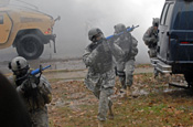 A four-man team approaches a building through the smoke and the rain to clear it after an ambush on their convoy during a Special Forces training event held at the Muscatatuck Urban Training Center in Indiana. The blue muzzles on their M4 assault rifles are modifications made to enable the weapon to shoot clay bullets, making the training more realistic. (U.S. Army photo by Spc. John Crosby)