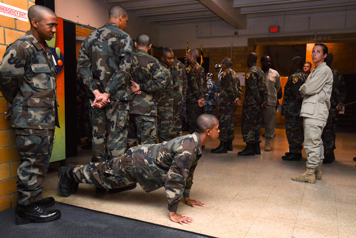 Malik Thompson knocks out pushups as Sgt. Drisana Lynch, right, a cadre member at the academy, keeps an eye on cadets while waiting for the start of graduation ceremonies. Graduation day doesn’t mean a reprieve from the rules, or the consequences that come from ignoring a cadre member’s instructions.