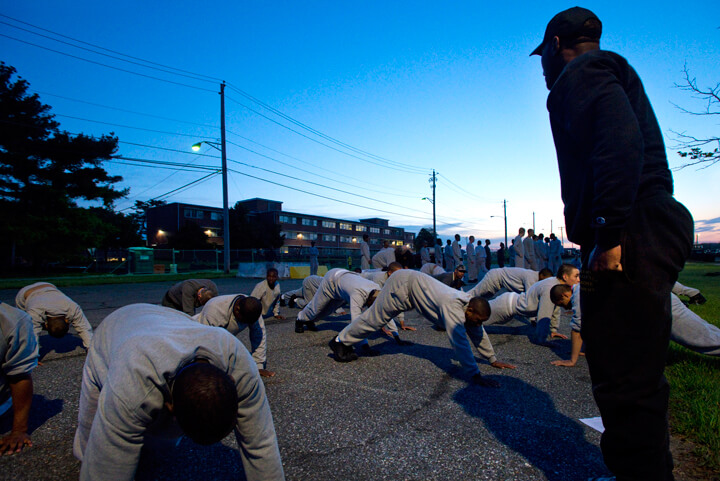 The glow of streetlights contrast against the pre-dawn sky as cadre members lead cadets in morning physical fitness training.