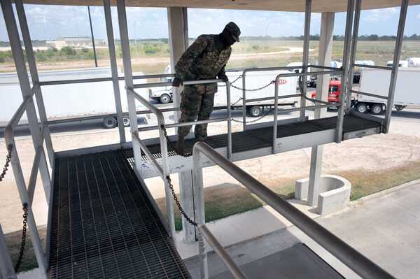 Watching from an overhead catwalk gives Spc. Kendhall Ingram, a truck driver with Headquarters and Headquarters Company, 536th BSB, an overhead view to spot for irregularities on top of trucks and trailers as they are driven into an inspection area below.
