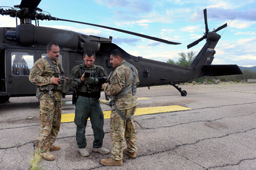 While on the ground at a small airfield south of Tucson, Ariz., Escobedo, right, reviews weather data with Chief Warrant Officer 2 Leo Tocchini, left, a fellow pilot, and acting Supervisory Border Patrol Agent William Colson. Flying OGS missions in Arizona often means staging near the border, making it easier to respond to calls from the field.